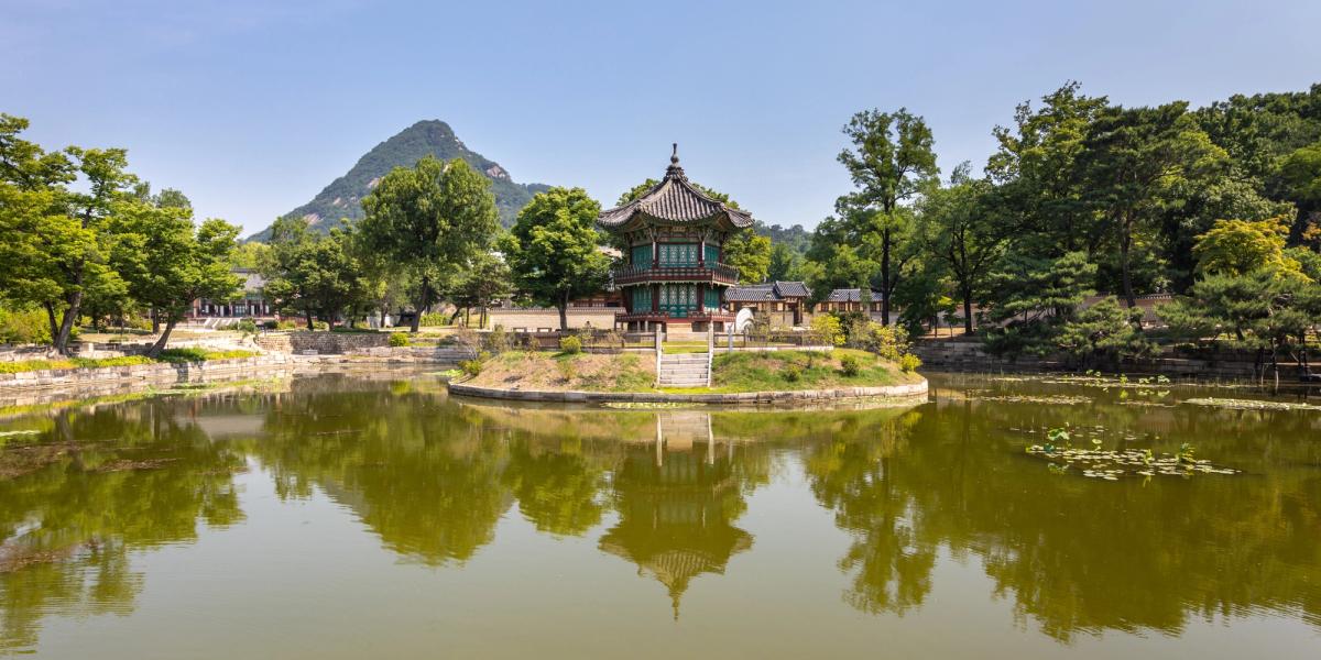 Hyangwonjeong Pavilion sitting on an island in its pond at Gyeongbokgung Palace under a clear blue sky.