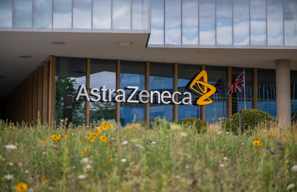 The image features the exterior of the AstraZeneca building, with a focus on its logo prominently displayed. The foreground is adorned with a variety of colorful wildflowers, creating a vibrant atmosphere. — Credit: Anthony Devlin/Getty Images for AstraZeneca