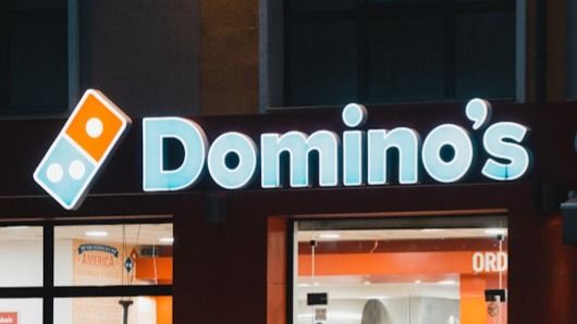 a group of people standing outside of a domino's store