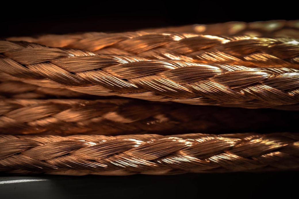 The image features a close-up view of braided copper wire with a shiny, reflective texture. The intricate weaving of the strands highlights the metal's conductivity and design used in various applications. — Credit: Photo by ERIK SETH on Unsplash