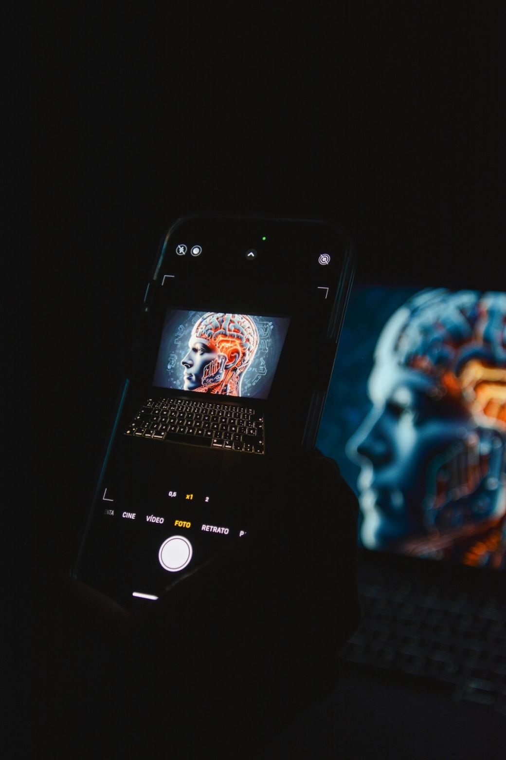 The image shows a close-up of a smartphone featuring a digital representation of a brain with neon circuits. The background exhibits a blurred outline of a human profile, suggesting themes of technology and artificial intelligence. — Credit: Photo by Aidin Geranrekab / Unsplash