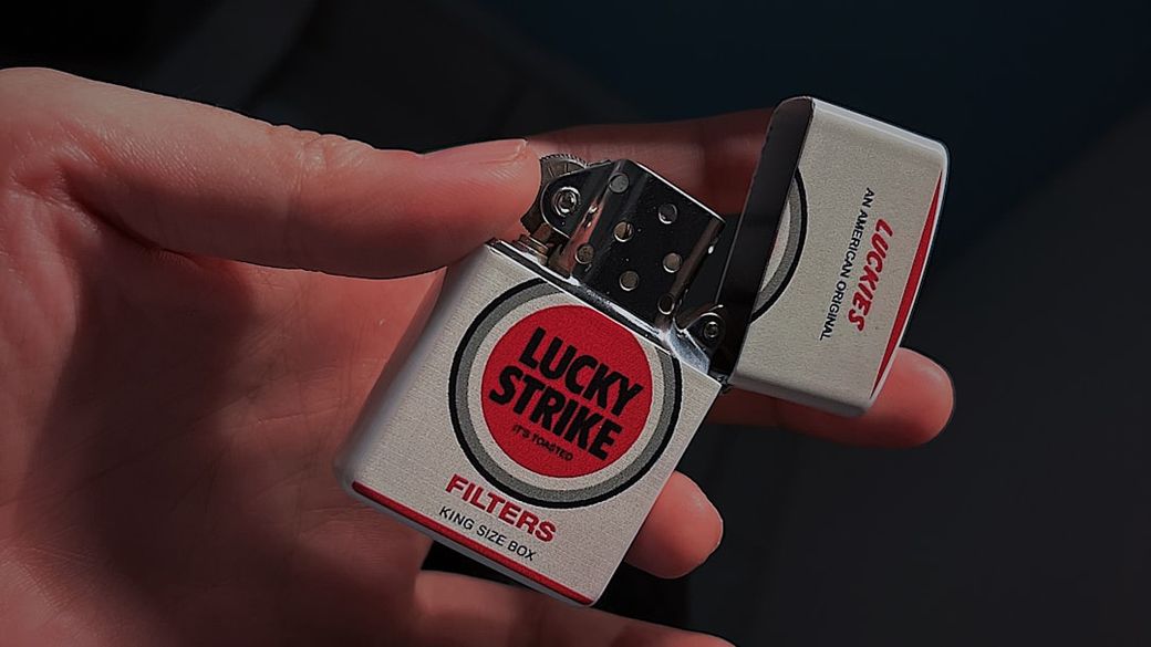 An individual holds a Lucky Strike cigarette pack with the flip-top lid open, displaying its bold red and white branding. The image highlights the product's design and aesthetic appeal. — Credit: Photo by Min Square_97 on Unsplash