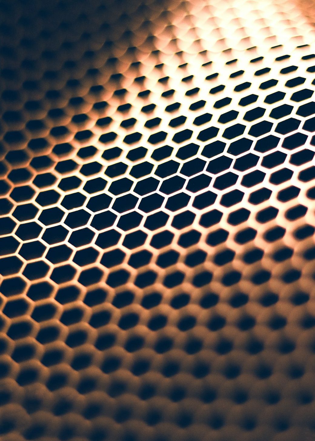 The image features a close-up view of a textured surface composed of hexagonal patterns, showcasing intricate geometric designs. The interplay of light on the surface creates a visually striking effect. — Credit: Photo by HY ART on Unsplash