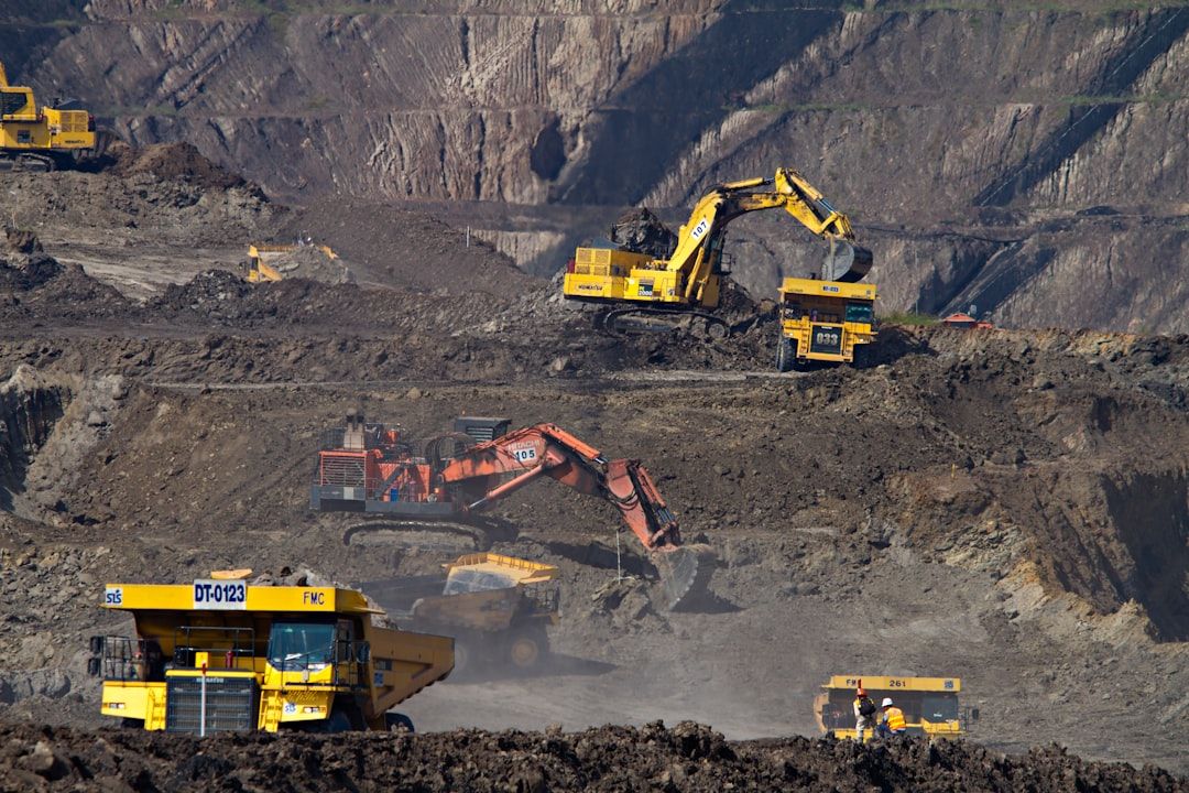 The image depicts heavy machinery at a mining site, highlighting various vehicles engaged in earthmoving operations. Large trucks and excavators are seen working on a rugged terrain, indicating active mining activities.