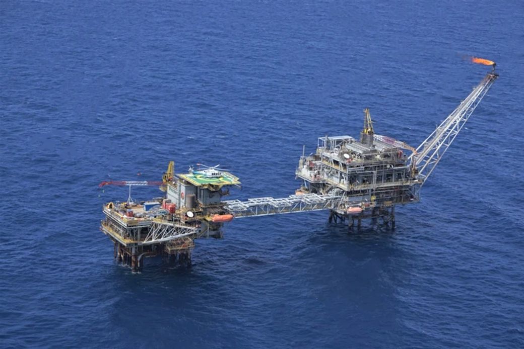 The image shows an offshore oil drilling platform situated in the open ocean. The platform is supported by legs submerged in water, reflecting the industrial activity involved in oil extraction.
