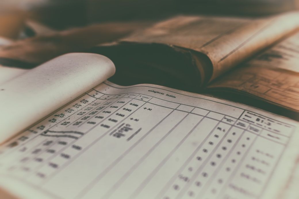 An open ledger or document displaying financial data, with printed columns and numeric entries. The background includes additional pages, hinting at historical records or accounting reports. — Credit: Photo by Denny Müller on Unsplash