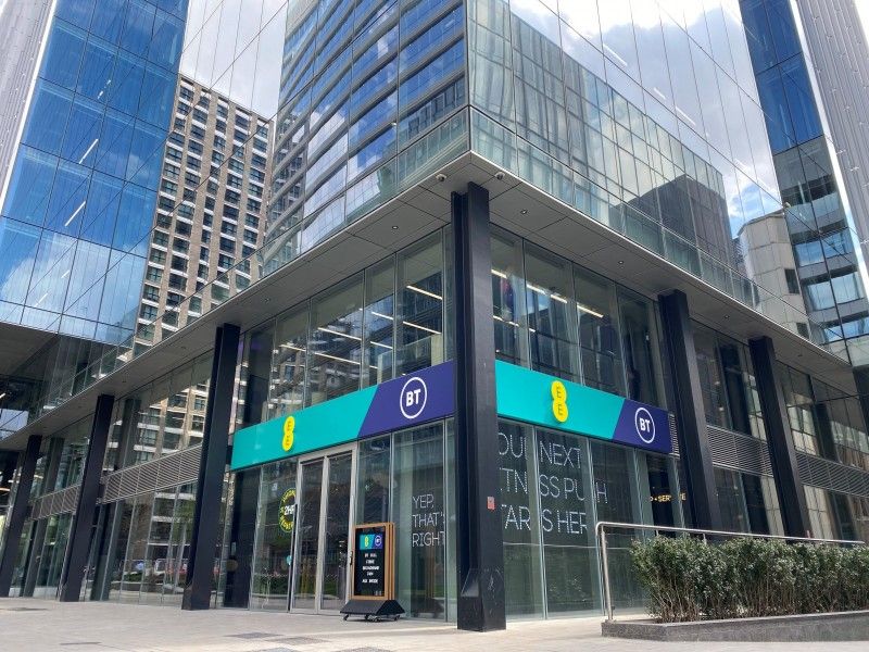 The image depicts a modern commercial building with large glass facades. The main entrance features a prominent green and blue logo, along with an advertising banner highlighting a message related to technology or services.