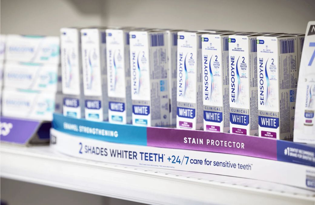 The image shows a shelf filled with various packages of Sensodyne toothpaste, prominently displaying multiple boxes with distinct branding and product details. The setting appears to be a retail space, specifically in the personal care or oral hygiene section.