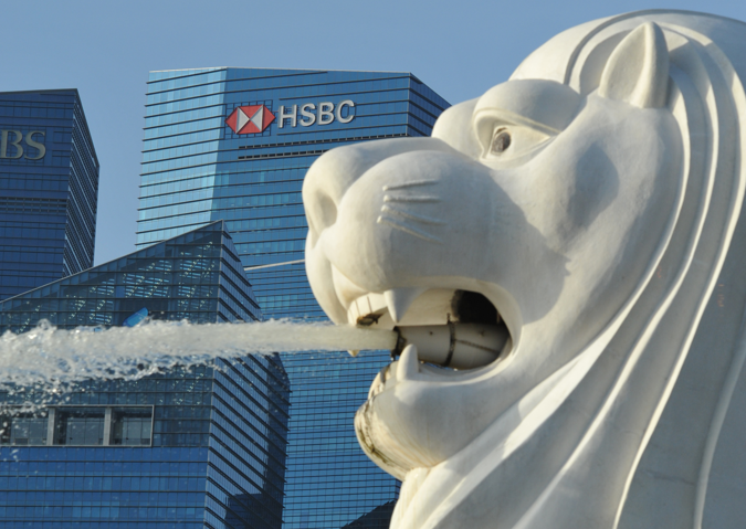 The image depicts the famous Merlion statue in Singapore, with water spouting from its mouth and prominent skyscrapers in the background. The HSBC logo is clearly visible on one of the buildings.