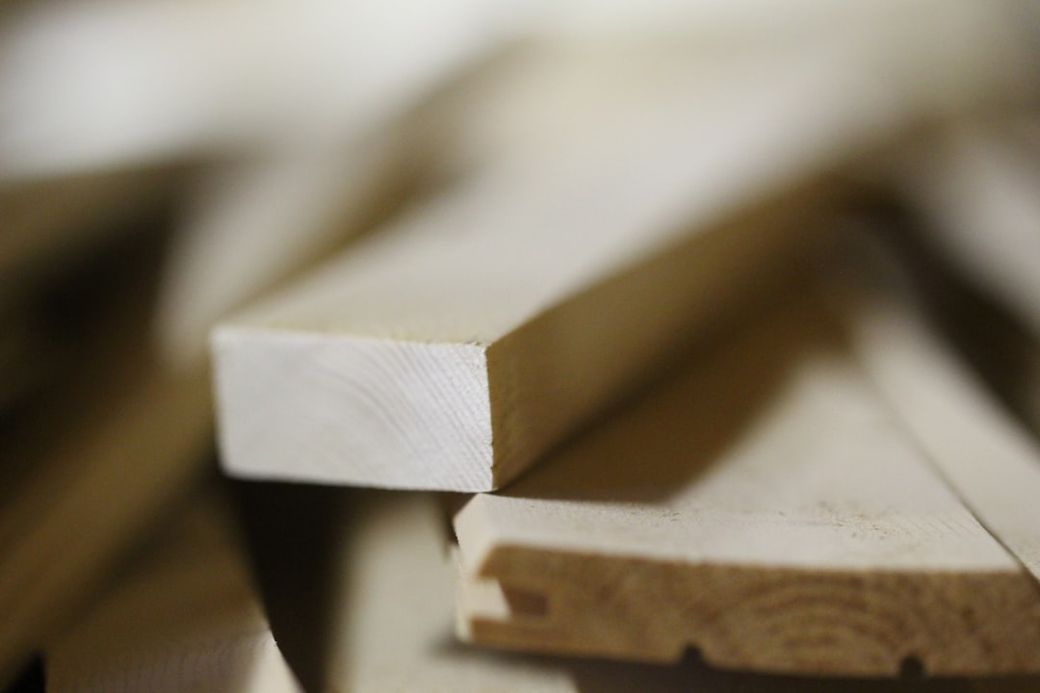 The image shows a close-up view of a stack of wooden planks, highlighting the texture and grain of the wood. The focus is on an individual plank in the foreground, with others slightly blurred in the background. — Credit: Photo by Anne Nygård on Unsplash