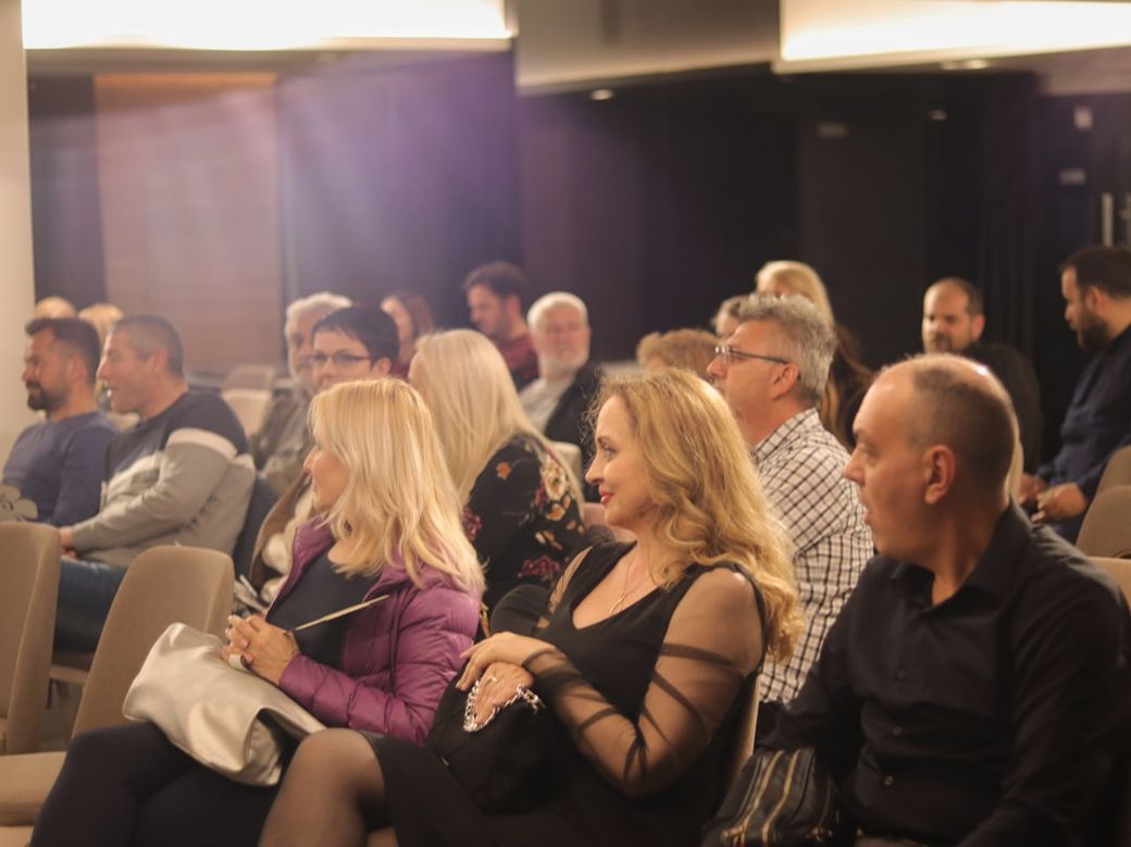 A diverse audience is seated in a modern conference setting, attentively listening to a speaker or presentation. The room is well-lit, showcasing a mix of individuals engaged in the event. — Credit: Photo by Anita Jankovic on Unsplash