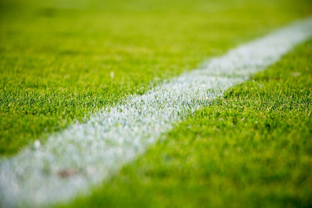 A close-up view of a well-maintained green soccer field showcasing a white boundary line. The lush grass is vibrant and the line is freshly painted, indicating readiness for a match. — Credit: Photo by Sandro Schuh on Unsplash