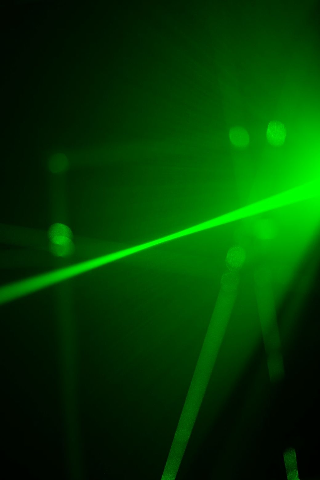 The image features a vibrant green laser beam cutting through a dark space, creating an abstract visual effect with light reflections. The atmosphere is dynamic and electrifying, emphasizing the power of laser technology. — Credit: Photo by Chayanin lawin on Unsplash