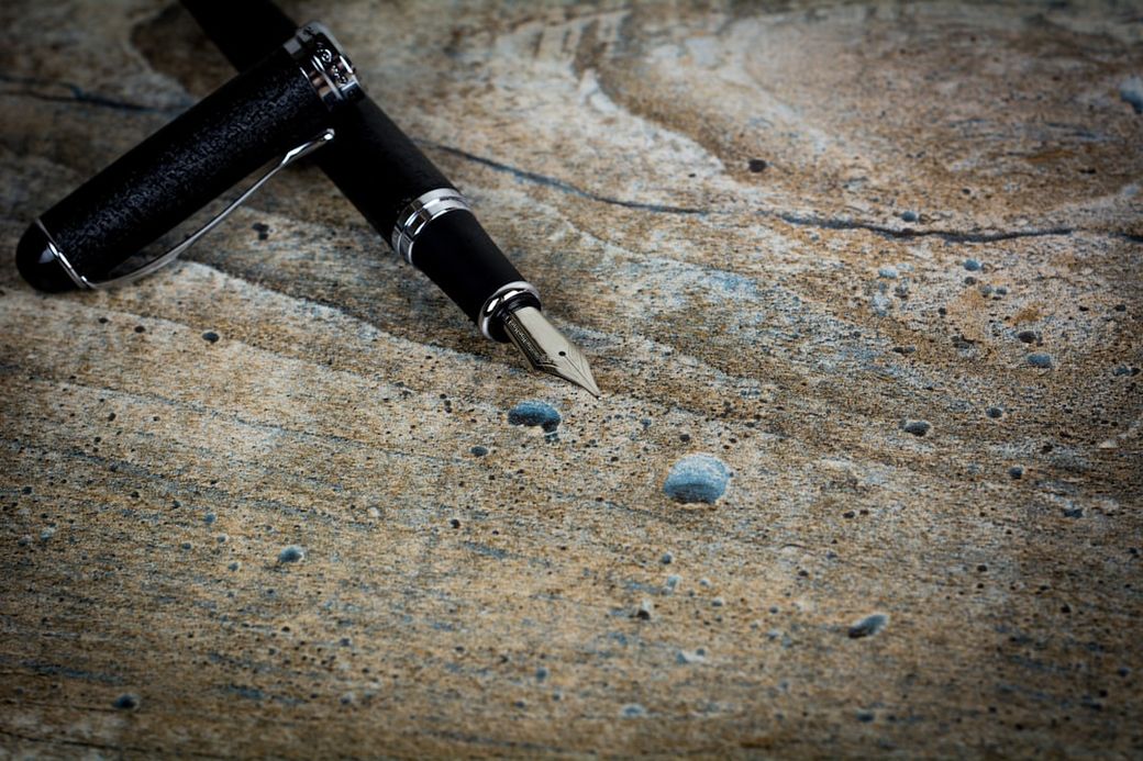 The image features a close-up view of a luxurious fountain pen resting on a weathered wooden surface. The pen's intricate details and the texture of the wood provide a contrast that highlights its elegance. — Credit: Photo by Bermix Studio on Unsplash