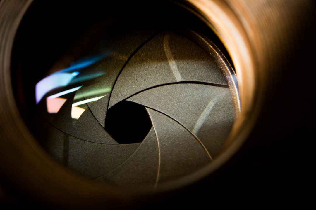 The image captures a close-up view of a camera lens aperture, showcasing the intricate blades that adjust the opening for light. The reflection and colors visible within the lens highlight the complexity of camera technology.