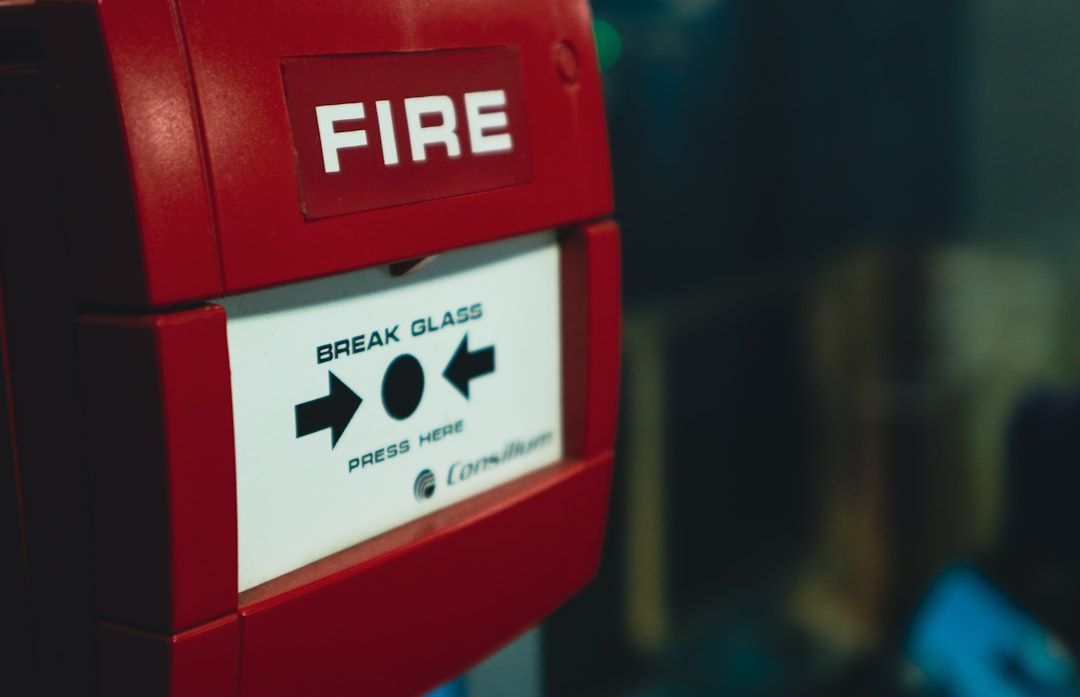 The image features a close-up view of a red fire alarm pull station with a clear 'FIRE' label and instructions for use. This safety equipment is typically found in public buildings to alert occupants in case of a fire emergency.