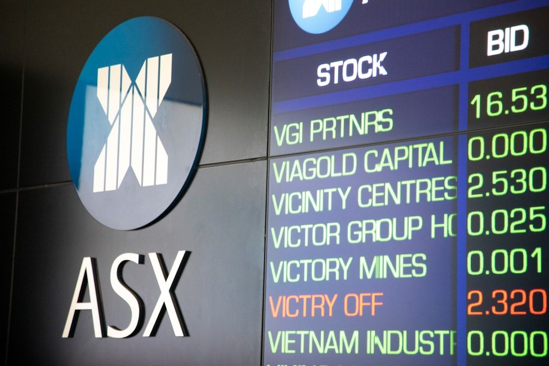The image depicts a digital display board showing stock market information from the Australian Stock Exchange (ASX). Visible are various stock names, their corresponding bid prices, and trading information.