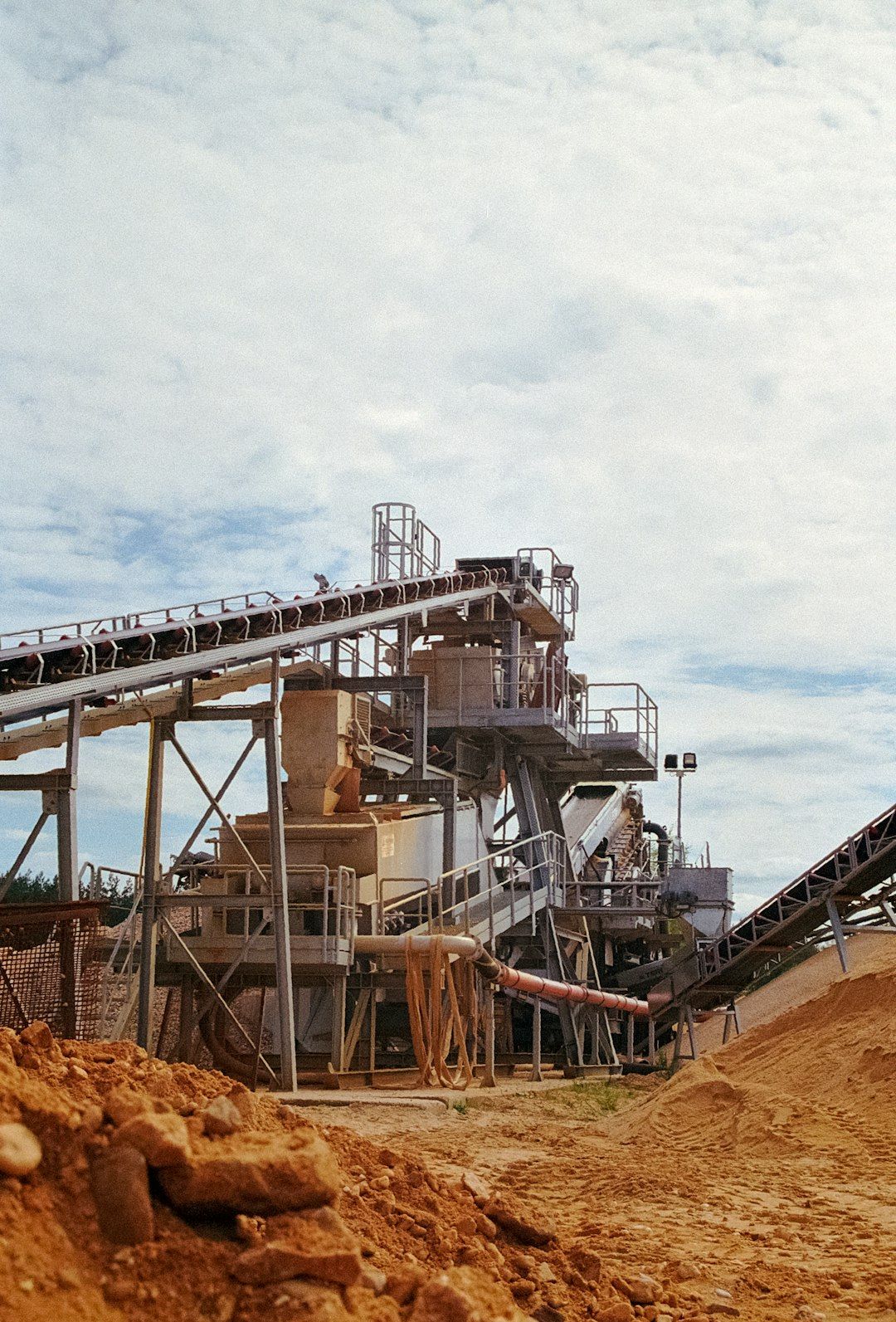 The image shows a large industrial facility with multiple conveyor belts and machinery, set against a cloudy sky. The facility appears to be involved in processing materials, possibly in a mining or construction context.