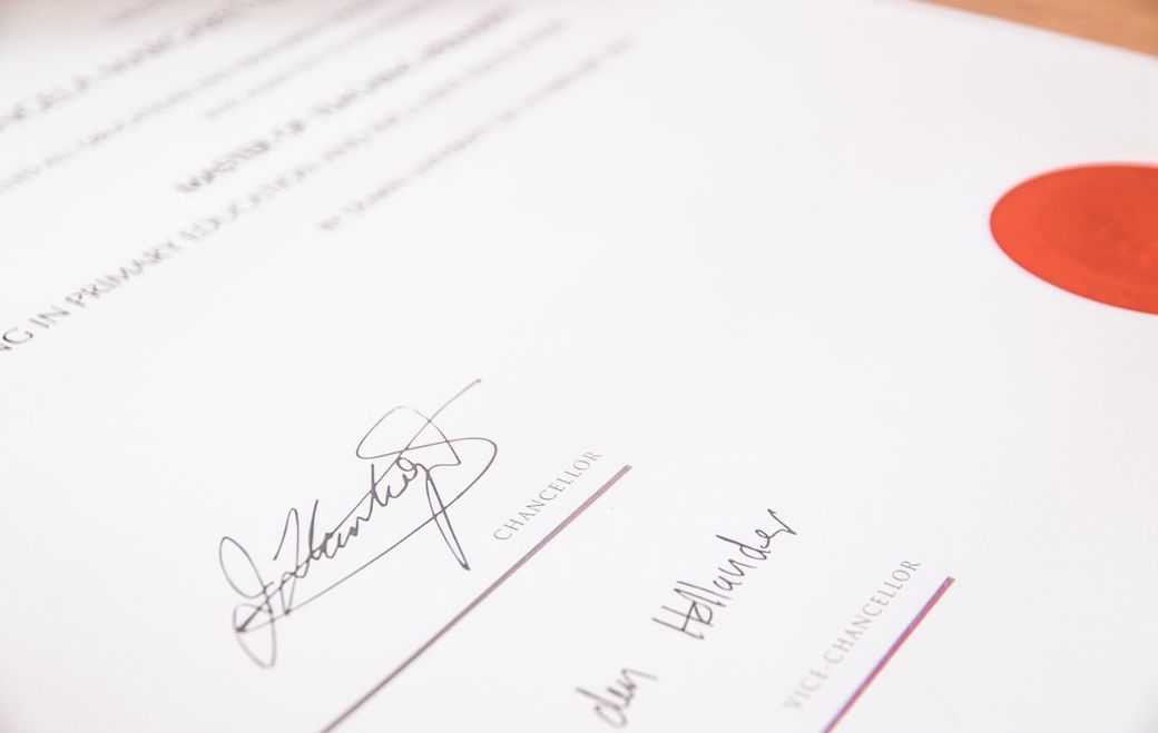 The image features a close-up view of a formal document, likely a certificate or diploma, displaying signatures and a prominent seal. The document is signed by individuals holding the titles of Chancellor and Vice Chancellor, suggesting an academic context. — Credit: Photo by Lewis Keegan on Unsplash