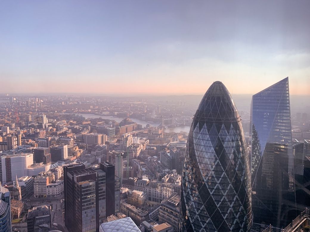 A panoramic view of a city skyline during early morning, showcasing modern architecture and a river. The foreground features distinctive glass buildings, with one shaped like an egg. — Credit: Photo by Alev Takil on Unsplash