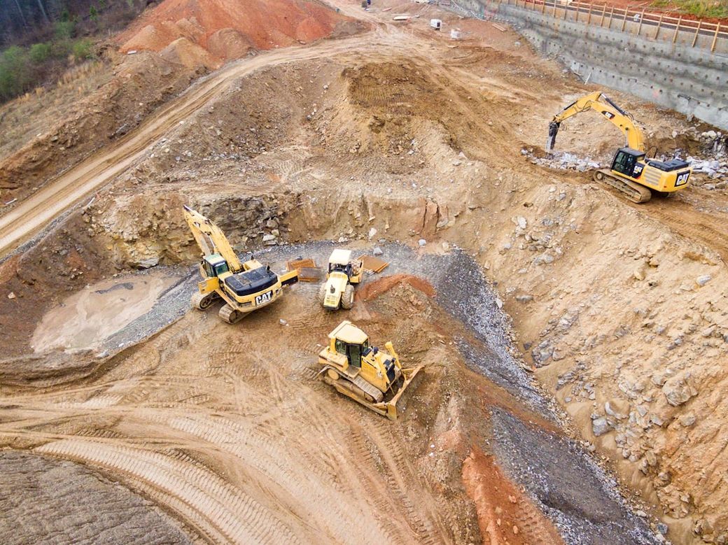 An aerial view of a construction site featuring heavy machinery operating on uneven terrain. The scene includes several bulldozers and excavators working on excavating and moving earth. — Credit: Photo by Shane McLendon on Unsplash
