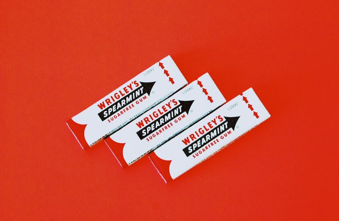 The image features three packs of Wrigley's Spearmint sugar-free gum arranged against a vibrant red background. The packaging displays the iconic branding clearly, emphasizing the product's flavor.