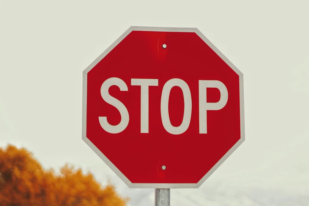 The image depicts a red stop sign prominently displayed against a neutral background. The bold white lettering clearly reads 'STOP', emphasizing the importance of traffic regulations. — Credit: Photo by Joshua Hoehne on Unsplash