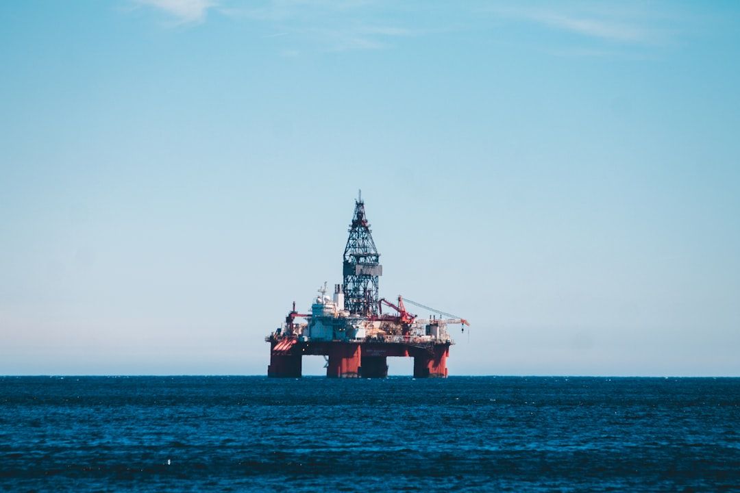 An offshore oil drilling rig stands prominently in the open sea against a clear blue sky. The structure is equipped with various machinery, indicative of its purpose in oil extraction and energy production.