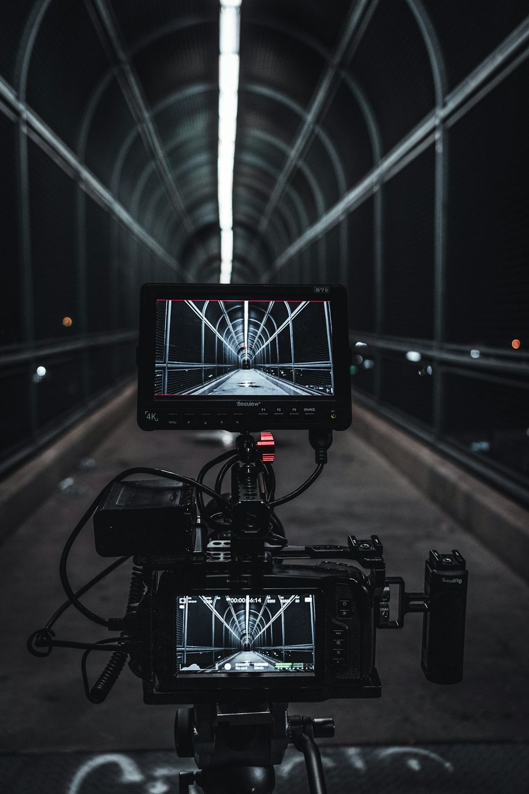 The image features a camera setup positioned at the end of a dimly lit tunnel, capturing a view of the tunnel's interior. The structure is illuminated by overhead lights, highlighting the geometric lines created by the tunnel's design. — Credit: Photo by Daniel Lincoln on Unsplash
