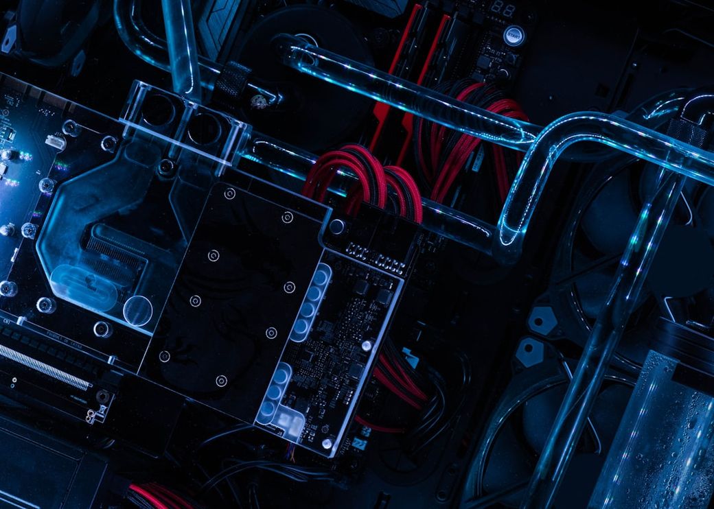 The image showcases an overhead view of a high-performance computer setup featuring intricate components like a graphics card and liquid cooling system. Vibrant blue lighting enhances the technological aesthetic of the hardware. — Credit: Photo by Cristiano Firmani on Unsplash