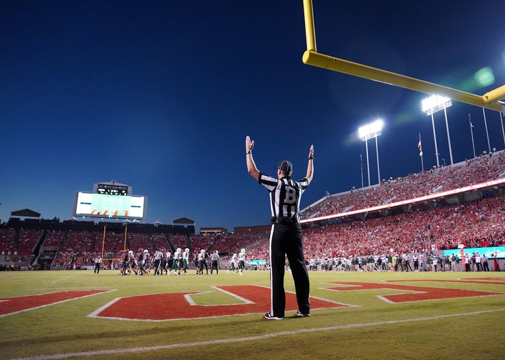 A football referee signals during a game at an outdoor stadium filled with spectators. The sky transitions from twilight to evening, enhancing the scene's excitement. — Credit: Photo by Gene Gallin on Unsplash