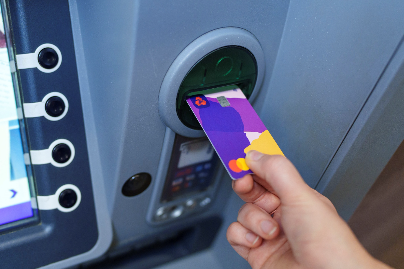 A person is using a colorful card at an ATM to withdraw cash. The ATM machine is modern with a digital display that includes various user interface options.