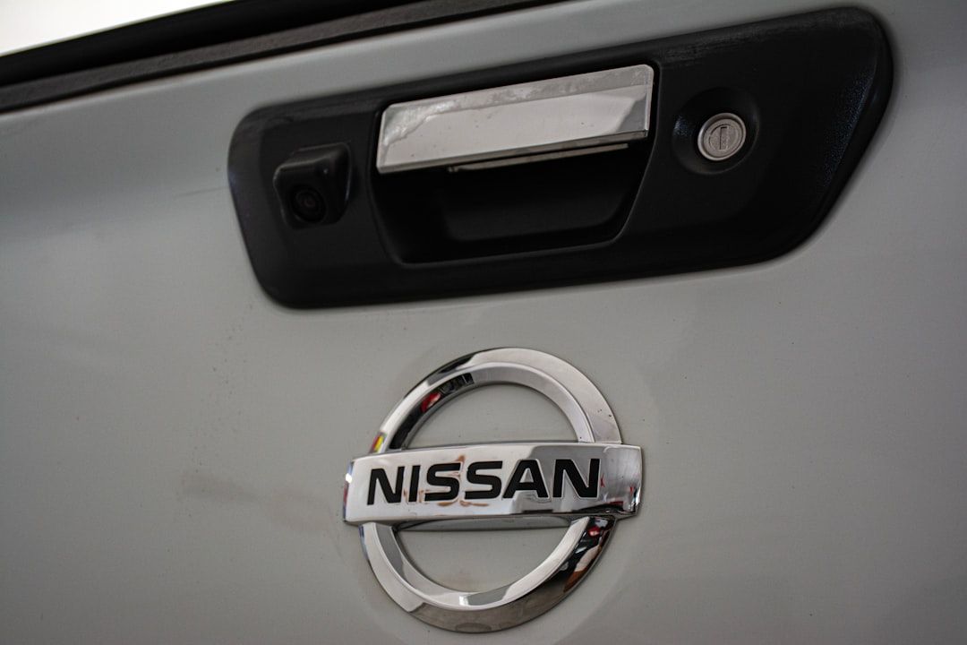 The image features the rear of a vehicle with a clear view of the Nissan logo and a door handle. The setting is likely a garage or workshop environment, emphasizing automotive design.