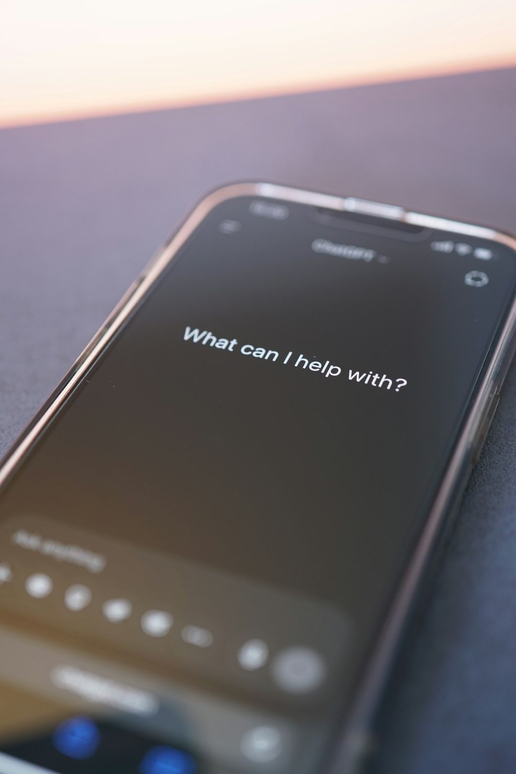 The image features a close-up view of a smartphone screen displaying a message that reads, 'What can I help with?'. The screen glows in a dark setting, emphasizing the text. — Credit: Photo by Tim Witzdam on Unsplash