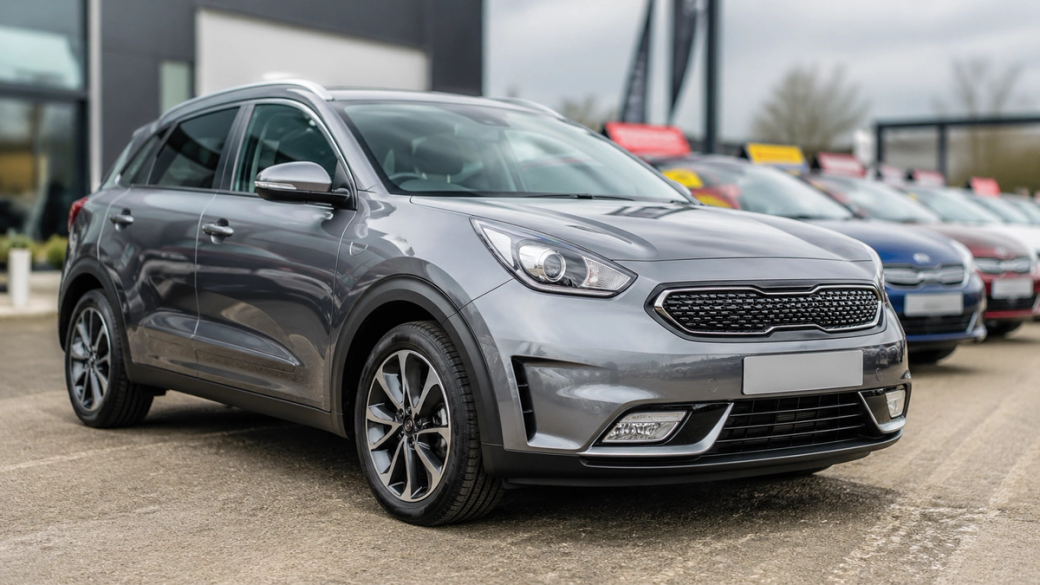 The image features a gray compact SUV parked prominently in the foreground, showcasing its sleek design and modern features. In the background, several other vehicles are lined up, indicating a car dealership setting.