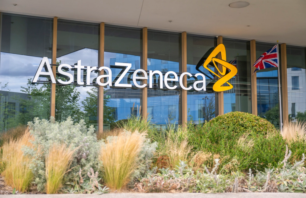 The image depicts the exterior of the AstraZeneca headquarters, showcasing a prominent logo displayed on the building's facade. The area is landscaped with greenery, providing a modern and inviting atmosphere. — Credit: Anthony Devlin/Getty Images for AstraZeneca
