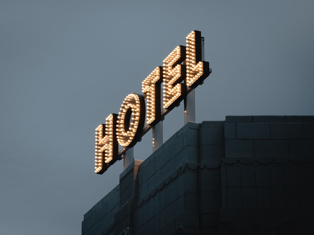 The image showcases a vintage hotel sign illuminated with light bulbs against a moody sky. The sign prominently displays the word 'HOTEL' in a bold and artistic font.