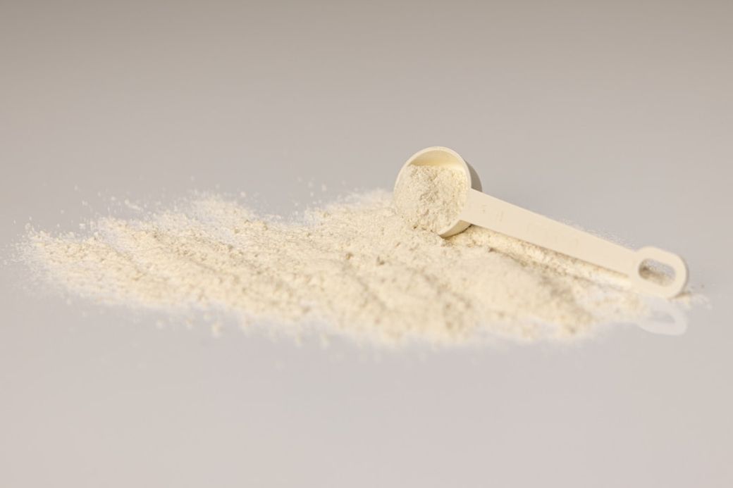 The image showcases a white scoop lying on a pile of fine powder. The powder appears to be a light-colored substance, possibly a protein or baking ingredient, set against a neutral background. — Credit: Photo by Alex Saks on Unsplash