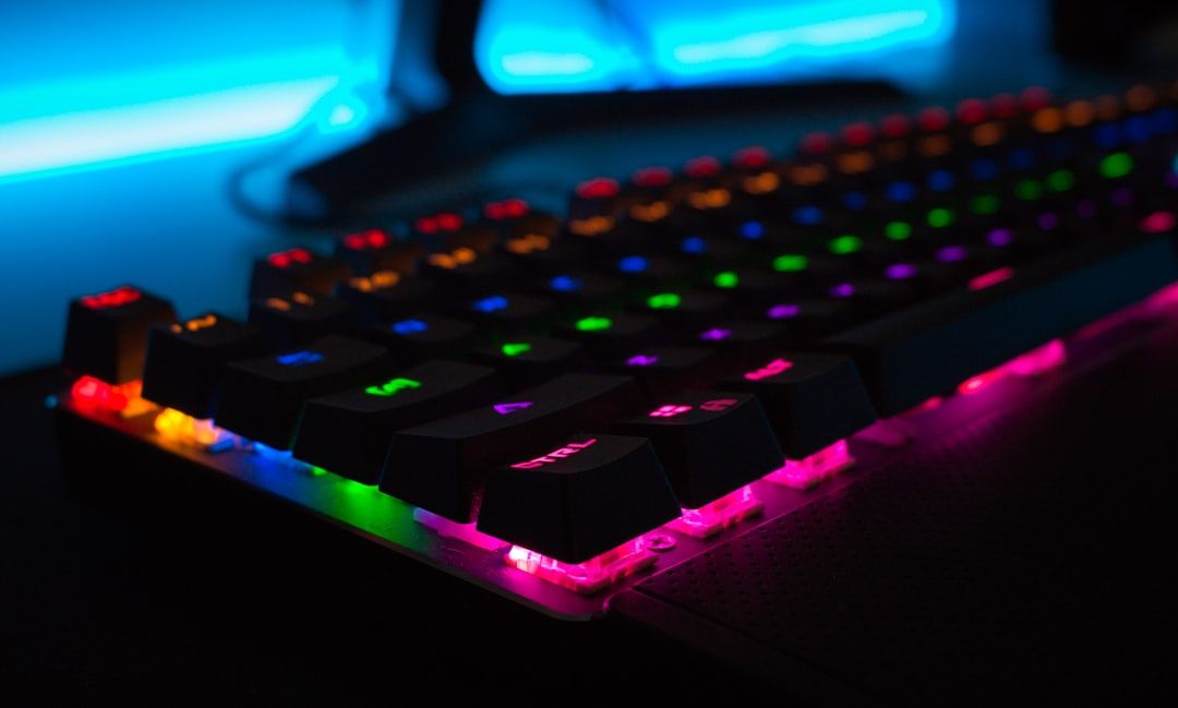 The image features a close-up view of a computer keyboard with vibrant RGB lighting. The keys are illuminated in various colors, creating a visually striking effect against a blurred background.