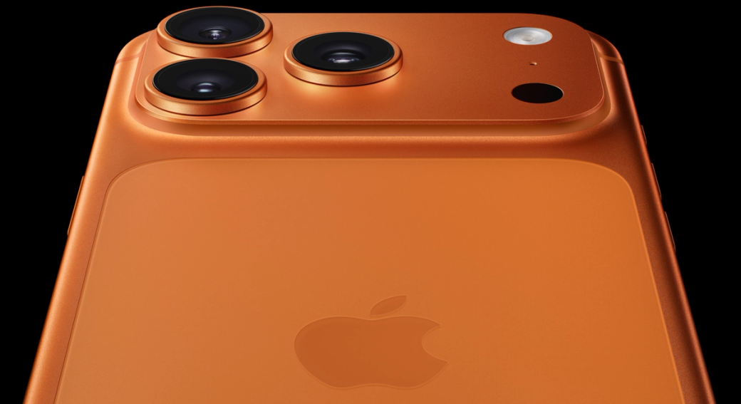 The image showcases the rear view of a smartphone featuring three cameras and a flash, set against a black background. The device is styled in a vibrant orange finish.