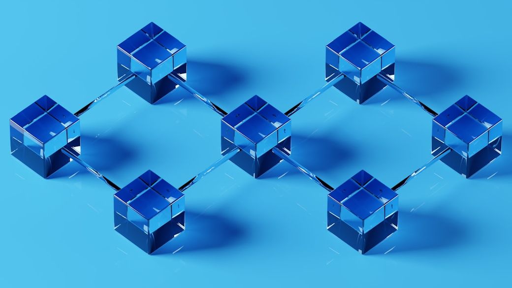 The image features a 3D representation of interconnected cubes arranged in a network structure, set against a blue background. This design symbolizes connectivity and data flow, often associated with blockchain technology. — Credit: Photo by Shubham Dhage on Unsplash