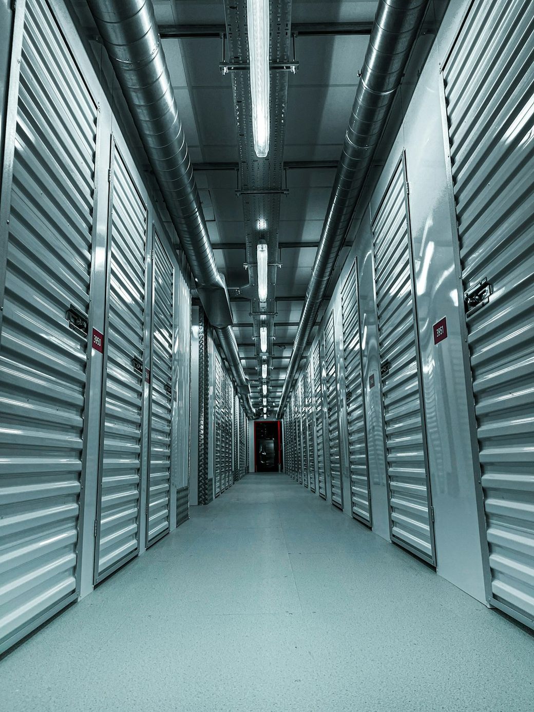 The image features a long corridor with storage unit doors on either side, characterized by metallic finishes and smooth flooring. The perspective emphasizes the depth of the hallway, leading to dim lighting at the far end. — Credit: Photo by Beatriz Reynolds on Unsplash