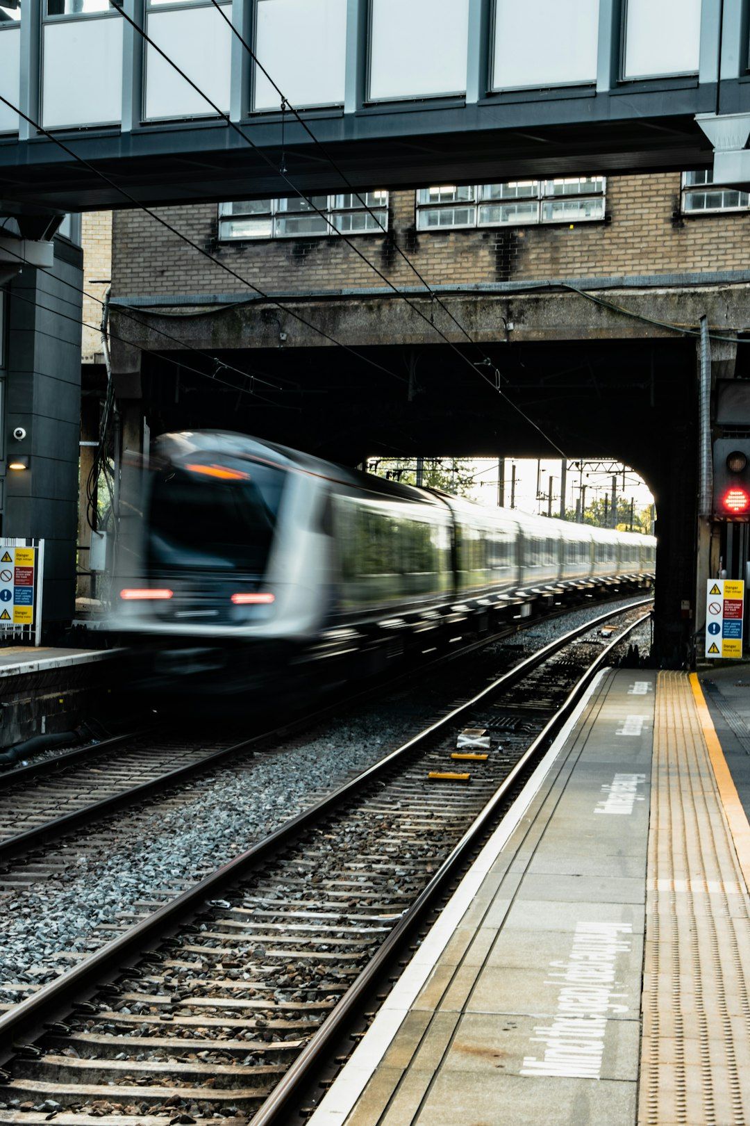 A blurred train speeds through an underground station as it approaches a platform. The scene is set in an urban railway environment, characterized by tracks and train infrastructure.