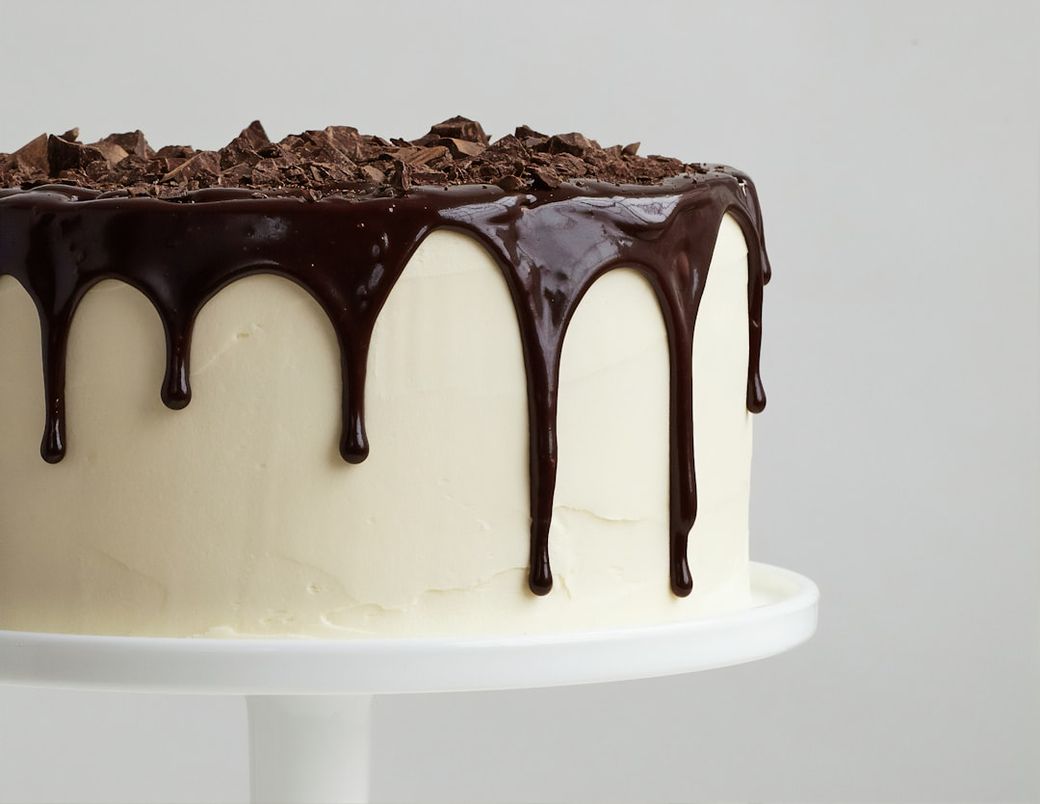 A close-up of a beautifully frosted cake with a glossy chocolate ganache dripping down the sides. The cake is topped with chopped chocolate pieces, creating an appealing dessert presentation. — Credit: Photo by American Heritage Chocolate on Unsplash