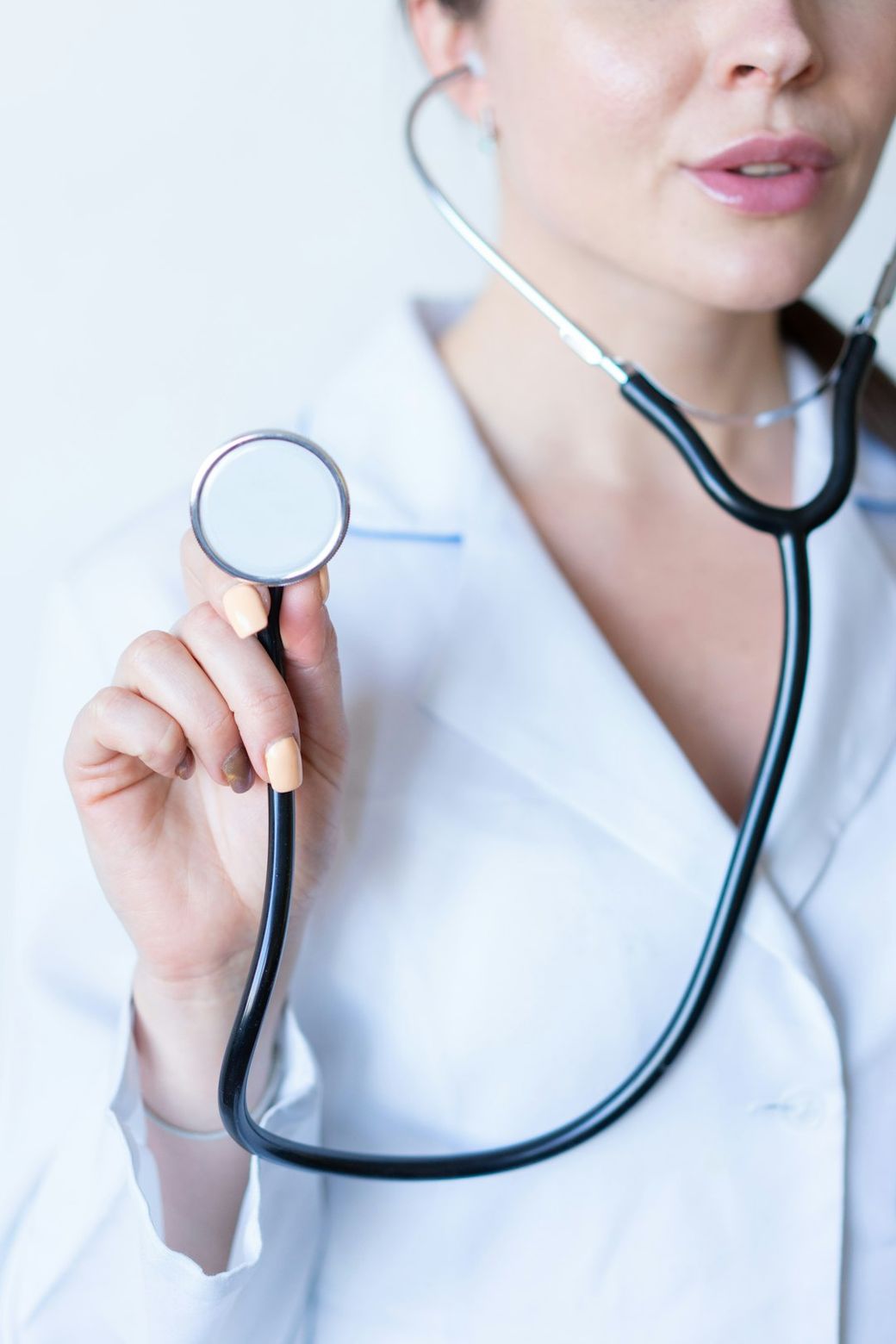 A healthcare professional holds a stethoscope, symbolizing the role of doctors in patient care. The image focuses on the upper body of the individual wearing a white lab coat. — Credit: Photo by Alexandr Podvalny on Unsplash