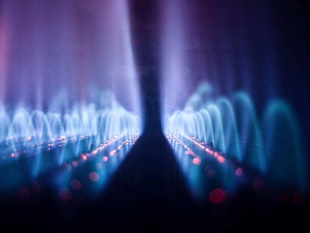 The image features abstract waves of light in hues of blue and purple, creating a visual representation of energy and flow. The patterns suggest a dynamic movement that could symbolize technology or scientific concepts. — Credit: Photo by Sugarman Joe on Unsplash