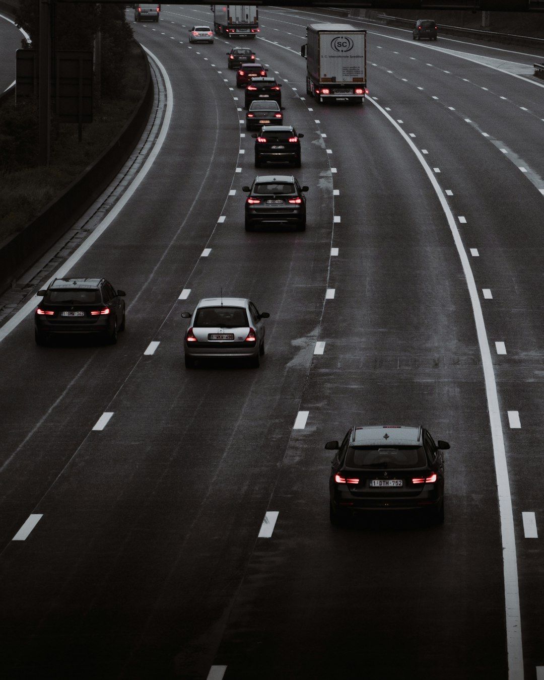 A view of a multi-lane highway with several vehicles traveling in the same direction. The road is wet, suggesting recent rain, and the scene is taken from an elevated perspective.