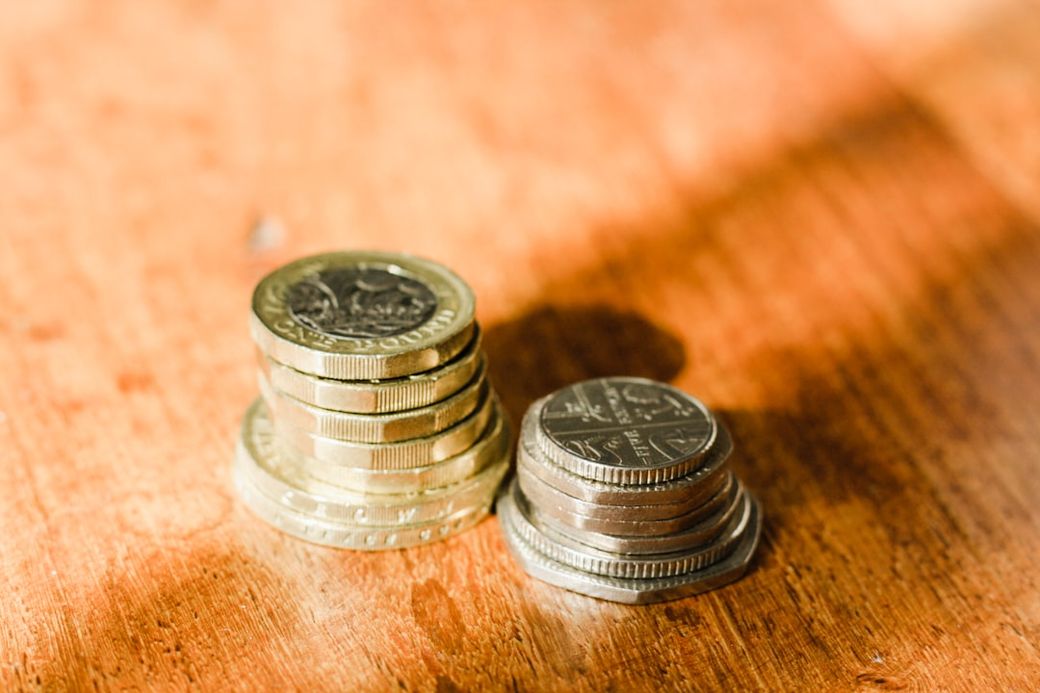 The image depicts a close-up view of stacks of coins arranged on a wooden surface. The coins vary in size and denomination, highlighting a focus on currency and finance. — Credit: Photo by Sarah Agnew on Unsplash