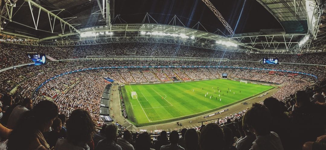 A panoramic view of a crowded stadium during a football match, showcasing enthusiastic fans and players on the pitch. The atmosphere is electric as the game unfolds under the stadium lights.