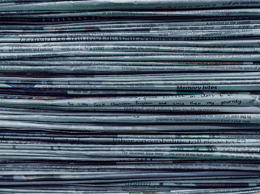 A stack of newspapers with various articles visible. The papers are printed in black and white, showcasing headlines and segments of text that suggest coverage of diverse topics.